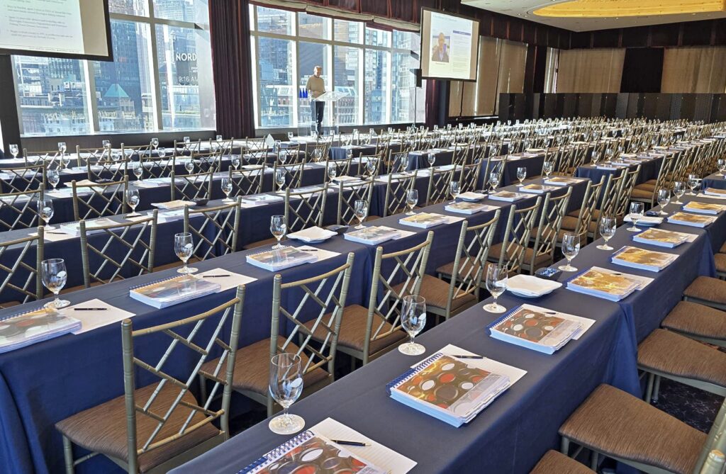 A large prepared meeting space in New York City with many rows of tables and chairs, and a thick, tabbed booklet printed and bound by ABG Print in front of each